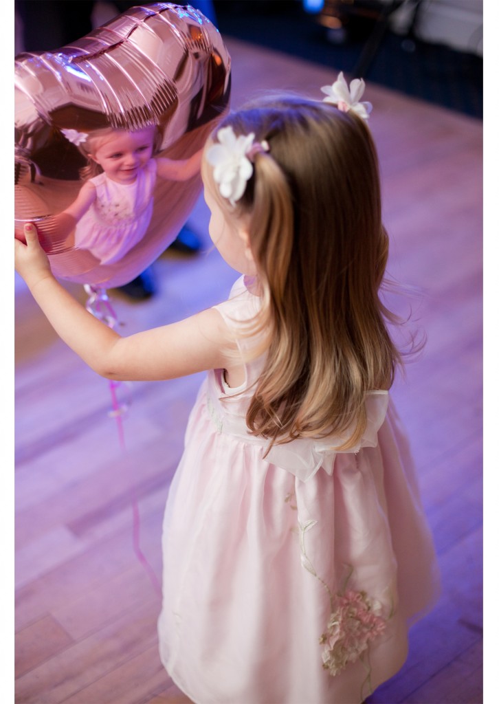 A little girl looks at her reflection in a balloon during a wedding reception