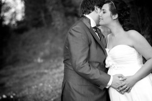 A pregnant bride is embraced by her groom